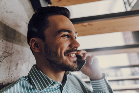 Jolly young man is chatting on phone indoorsの写真素材