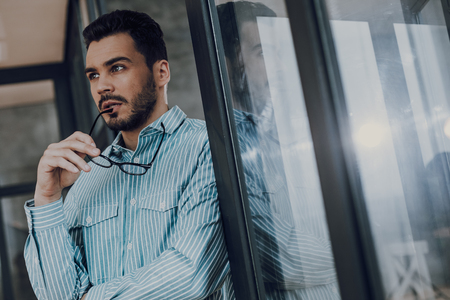 Pensive young bearded man with glasses indoorsの写真素材