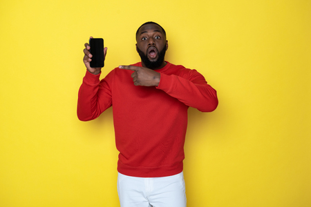 Waist up of surprised African man holding smartphone in armsの写真素材