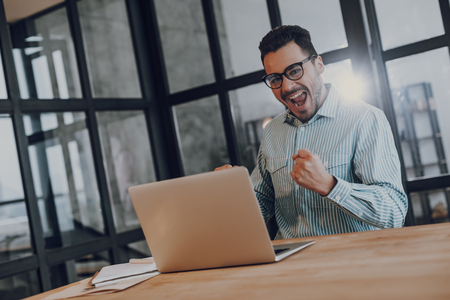 Excited man succeed in working on laptopの写真素材