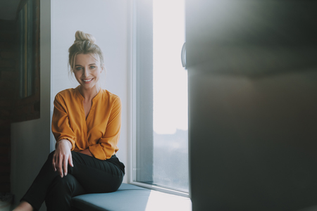 Cheerful lady sitting on the window sill and smilingの写真素材