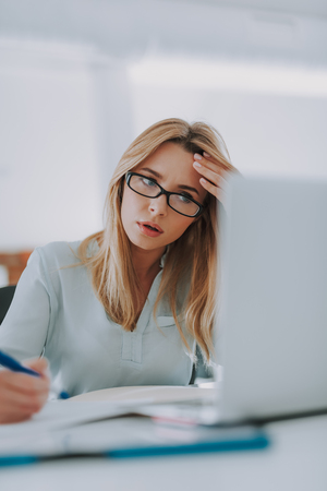 Busy woman touching her forehead and looking at the laptopの写真素材