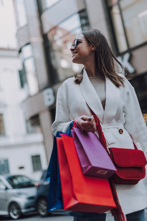 Charming young woman with shopping bags standing on the streetの写真素材