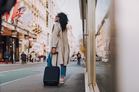 Stylish afro american girl with travel trolley bag standing on the streetの写真素材