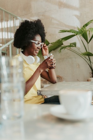 Waist up of beautiful African woman having rest in cafeteriaの写真素材