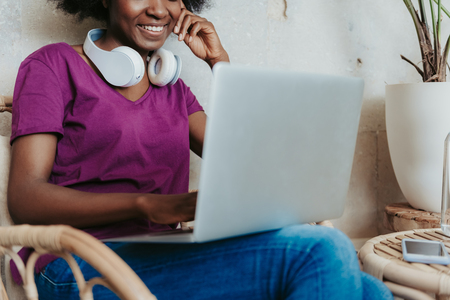 Happy African woman with headphones on shoulders surfing the Internet in cafeの写真素材