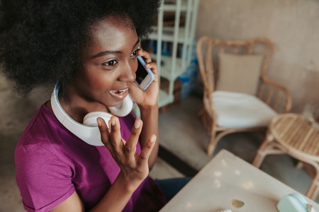 Close up of stylish African woman with headphones having chat on smartphoneの写真素材