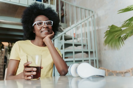 Low angle of smiling African woman having rest in cafeteriaの写真素材