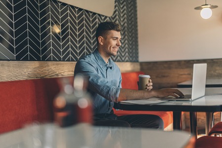 Smiling young man using modern laptop in the cafeの写真素材