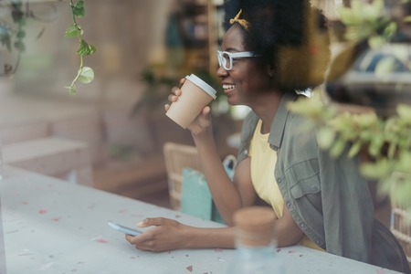 Side view of happy African lady having rest in cafeteriaの写真素材