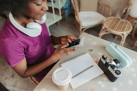 Close up of stylish African woman with headphones looking at screen of mobile phoneの写真素材