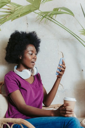 Waist up of shocked African woman wearing casual and looking at smartphone