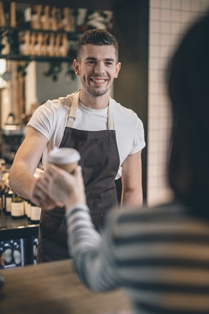 Waist up of friendly barista smiling to the cafe visitorの写真素材