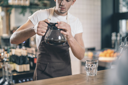 Careful barista looking at the glass coffee jug in his handsの写真素材