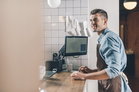 Cheerful barista smiling while standing in front of the bar counterの写真素材