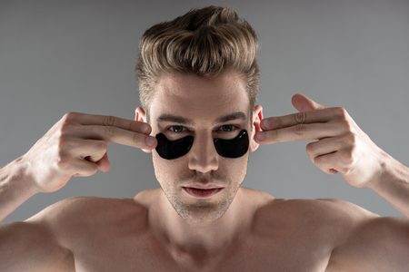 Handsome young man pointing at black under eye patchesの写真素材