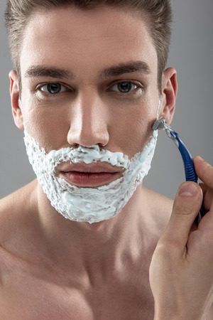 Attractive young man shaving with disposable razorの写真素材