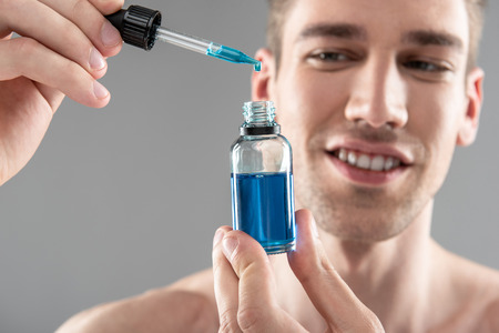 Attractive young man holding vitamin serum and smilingの写真素材