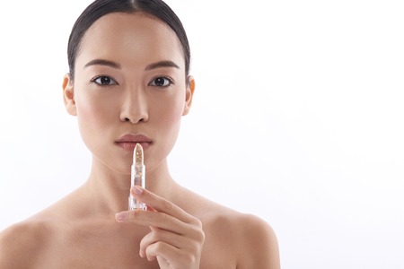 Serious Asian woman standing with lipstick in her handの写真素材