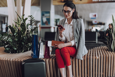 Relaxed woman is using mobile phone in airportの写真素材