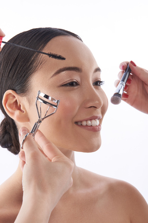 Hands of beauticians applying makeup on the face of Asian womanの写真素材