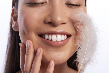 Close up of pleased woman with feather on her cheekの写真素材