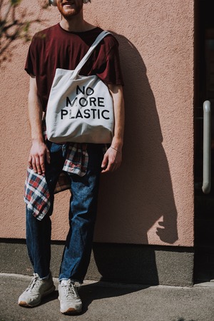 Young hipster man with eco bag leaning on wallの写真素材