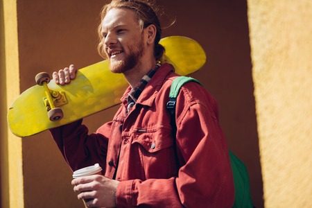 Smiling hipster man with coffee and skateboardの写真素材