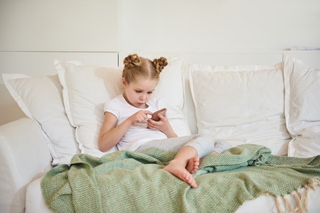 Cute little girl using smartphone at homeの写真素材
