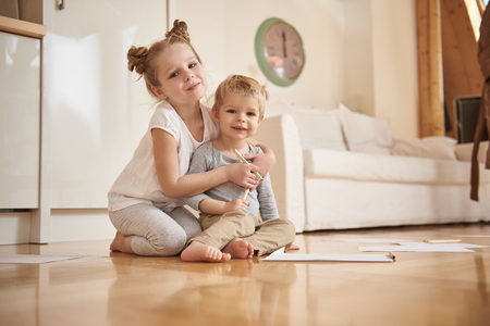 Adorable little girl hugging her brother from behind at homeの写真素材