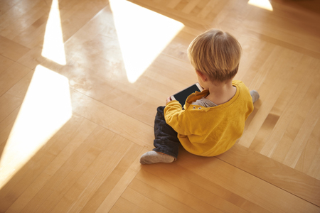 Cute little boy sitting on the floor and using cellphoneの写真素材