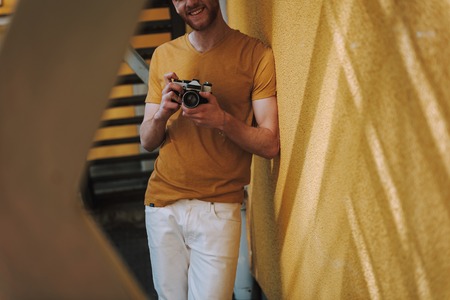 Young smiling man leaning on wall with cameraの写真素材