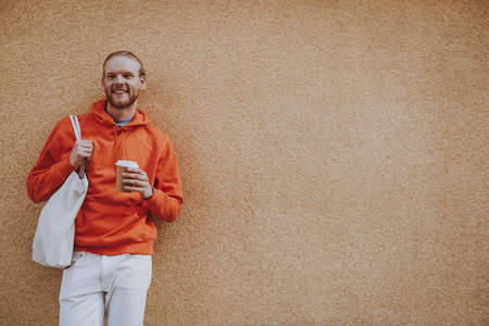 Happy red haired male leaning on wall with coffeeの写真素材