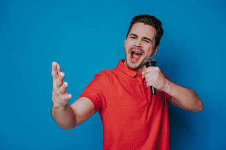 Waist up of Caucasian attractive man holding microphone in arms in studioの写真素材