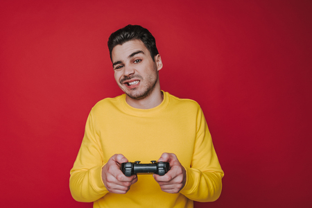 Half length of unpleasant guy squinting and holding joystick on red backgroundの写真素材