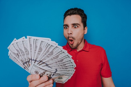 Waist up of unshaven shocked guy looking at money in arm indoorsの写真素材