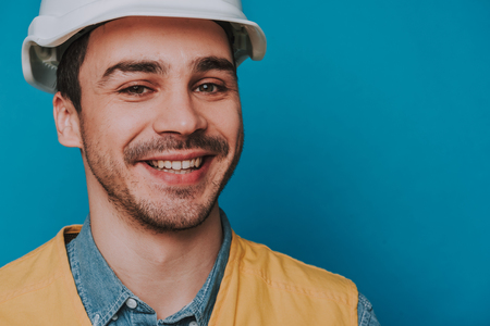 Cropped photo of happy guy wearing helmet and vest on blue backgroundの写真素材