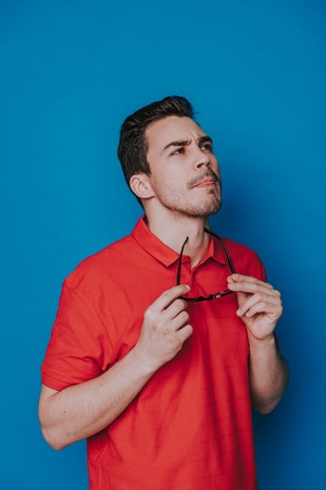 Close up of pensive Caucasian guy looking aside on blue backgroundの写真素材