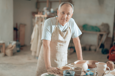 Waist up of handsome mature craftsman looking at camera in workshopの写真素材