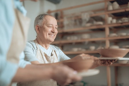 Low angle of happy craftsman looking at his ceramic bowl in workshopの写真素材