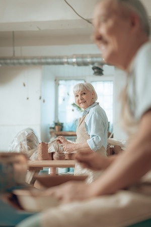 Waist up of smiling elderly craftswoman painting earthenware in potters studioの写真素材