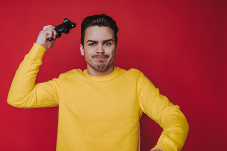 Half length of frowning brown-haired guy holding joystick on red backgroundの写真素材