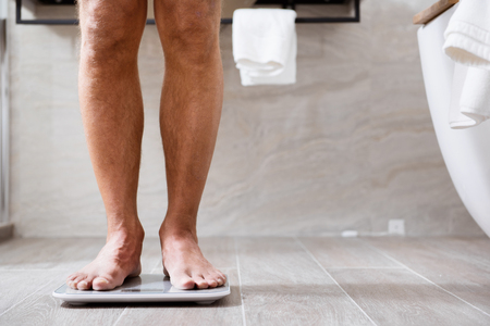 Close up of the man being barefooted in bathroom and using scalesの写真素材