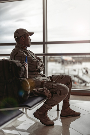 American soldier in camouflage sitting near window and looking through itの写真素材