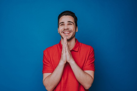 Low angle of happy handsome unshaven man praying on blue wallの写真素材