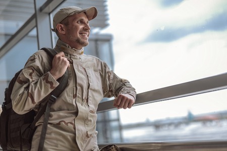 Low angle of smiling American soldier in camouflage looking at the windowの写真素材