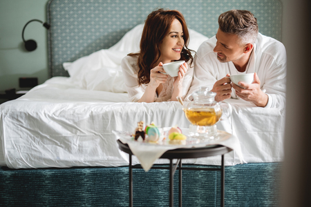 Lovely couple lying on the bed and drinking teaの写真素材