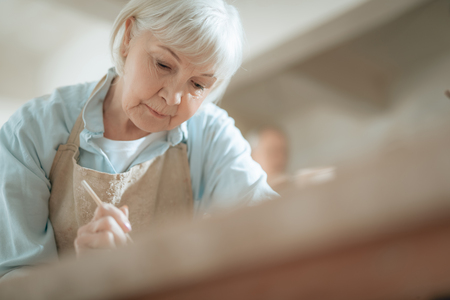 Cropped photo of elderly craftswoman painting decorative plate in workshopの写真素材