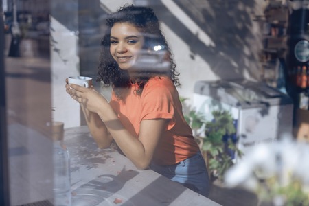 Happy young girl is enjoying coffee in cafeの写真素材