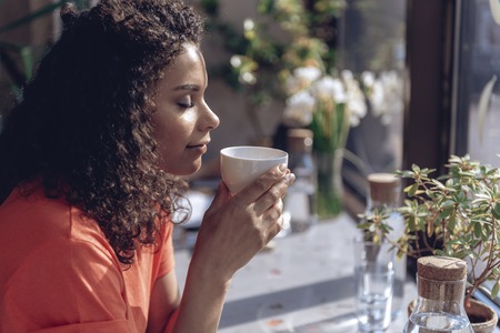 Young woman is enjoying aroma of hot drink indoorsの写真素材